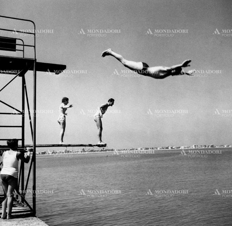 Two couples cool down, jumping from the diving board on the seafront of the Romagna Riviera. Rimini (Italy). SPECIAL FEE - CONTACT US FOR NOT EDITORIAL USAGE