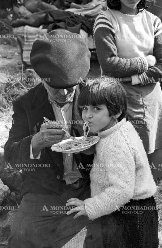A little Italian girl who survived the Belice earthquake eating pasta embarked on by a man. Sicily, January 1968 SPECIAL FEE  - CONTACT US FOR NOT EDITORIAL USAGE