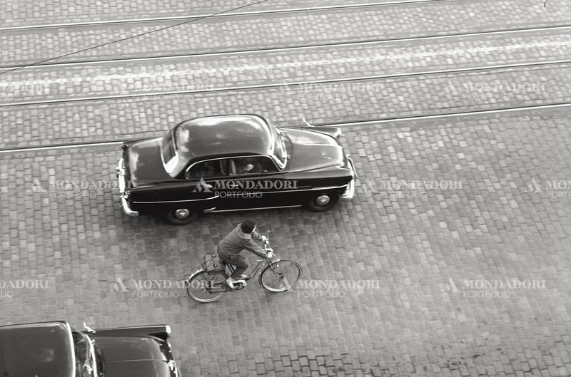 Cyclist travelling alongside a car. Germany, 1950s SPECIAL FEE  - CONTACT US FOR NOT EDITORIAL USAGE