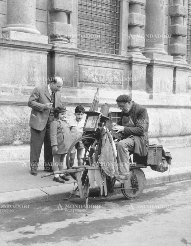 A knife grinder working under the gaze of two children. Milan, 1950s SPECIAL FEE  - CONTACT US FOR NOT EDITORIAL USAGE